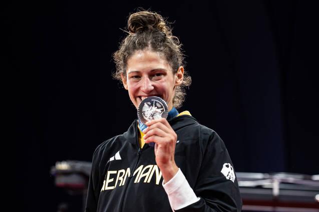 Sportlerin in schwarzer Jacke h&auml;lt stolz eine Silbermedaille vor ihrem Gesicht und l&auml;chelt auf einer B&uuml;hne.