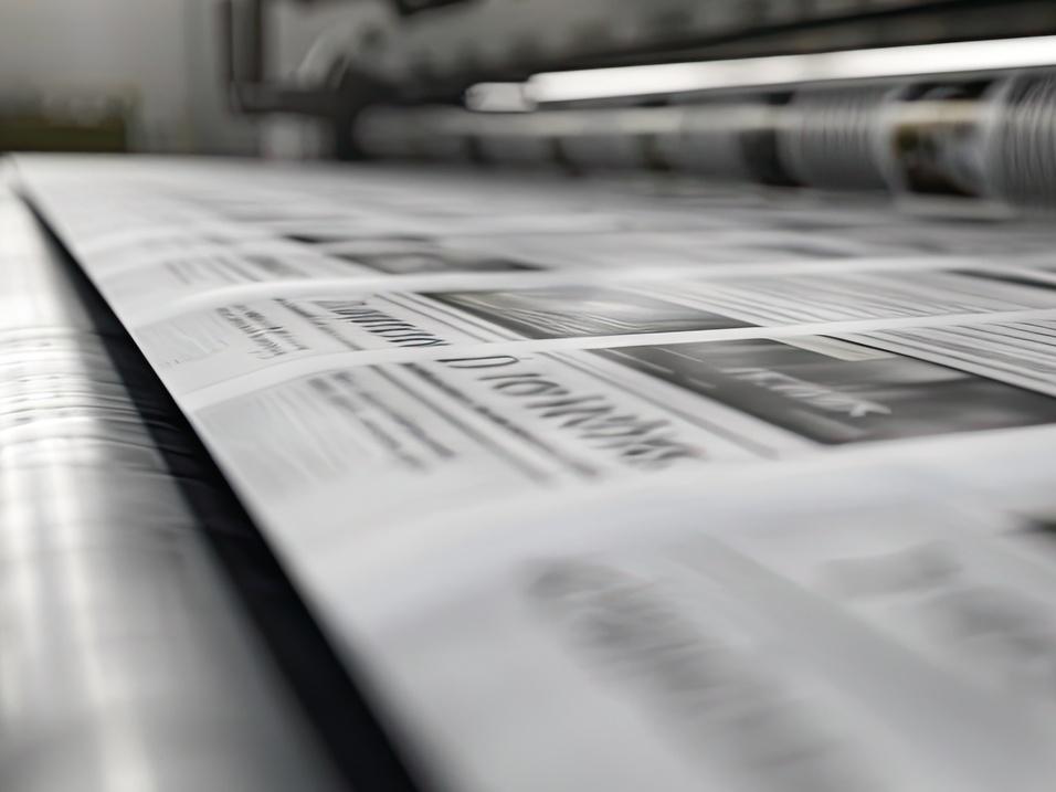 Nahaufnahme von gedruckten Zeitungsseiten, die auf einem Drucktisch in einer Druckerei ausgelegt sind.
