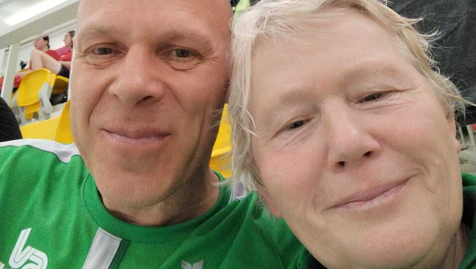Nahaufnahme eines Mannes und einer Frau, beide in grünen Sportjacken, die lächelnd in die Kamera blicken.
