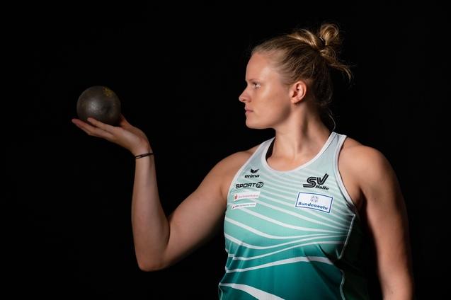 Athletin h&auml;lt eine Kugel in der Hand, schaut konzentriert zur Seite, schwarze Hintergrundbeleuchtung.