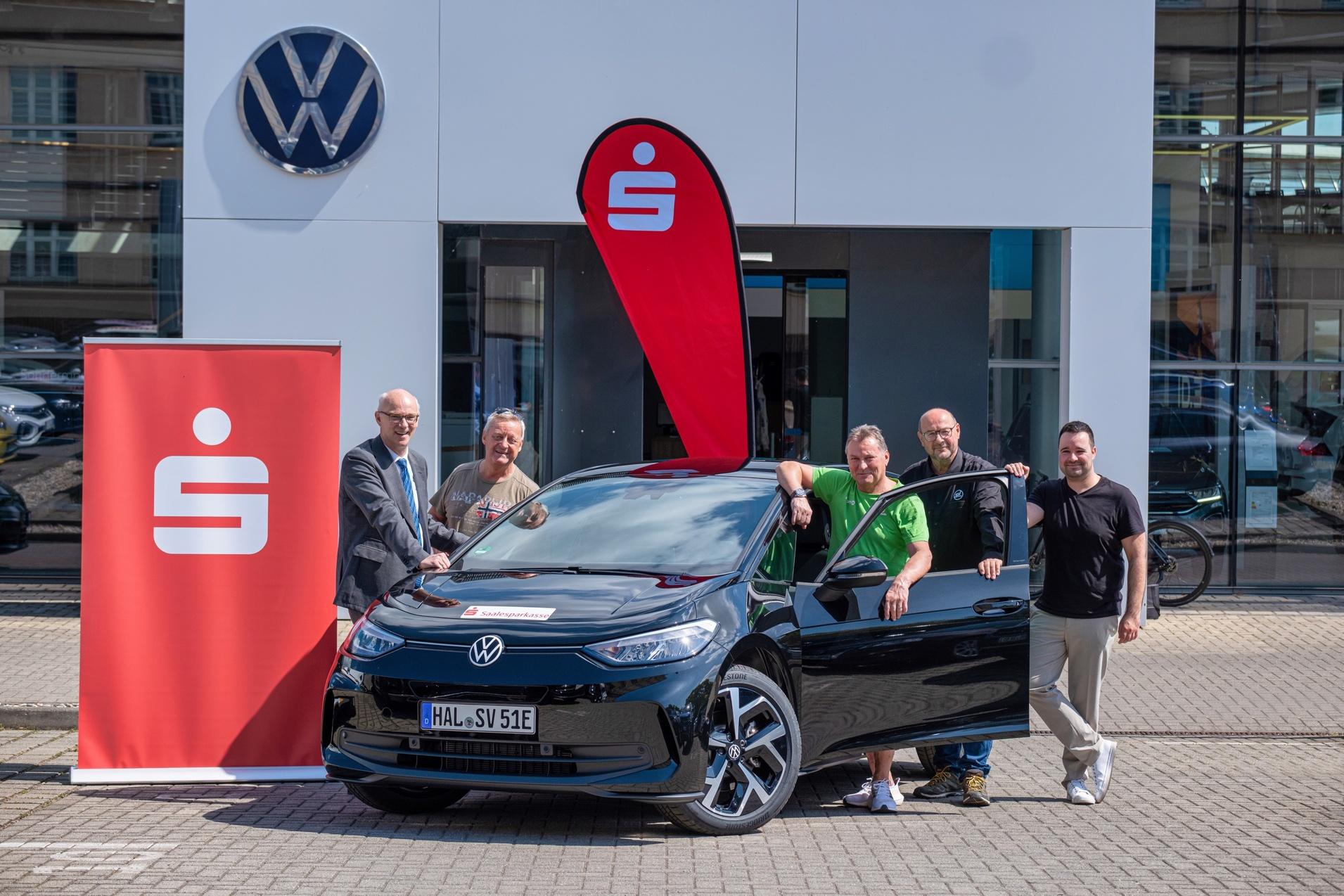Gruppe von f&uuml;nf Personen steht um einen schwarzen Volkswagen ID.4 vor einem Autohaus mit Logo im Hintergrund.
