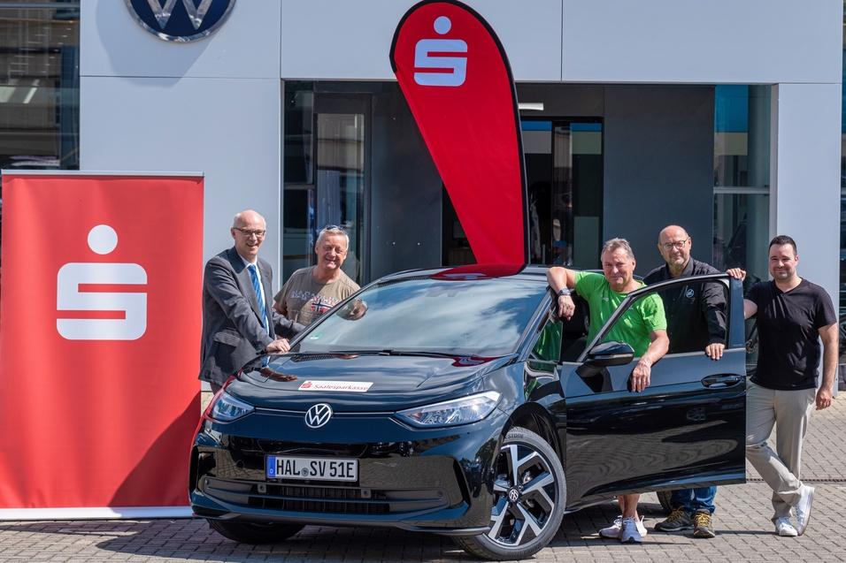 Gruppe von fünf Personen steht um einen schwarzen Volkswagen ID.4 vor einem Autohaus mit Logo im Hintergrund.