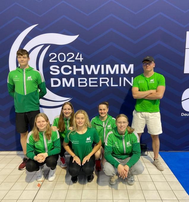 Gruppenselfie von sechs Schwimmern in grünen Trikots vor einem Hintergrund mit dem Schriftzug „2024 SCHWIMM DM BERLIN“.