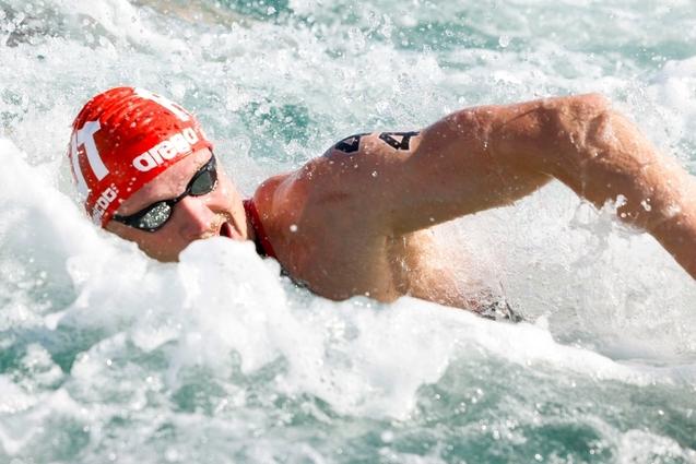 Schwimmer im roten Badekappe und Sonnenbrille, der in Wellengängen schwimmt und dabei kräftig stößt.