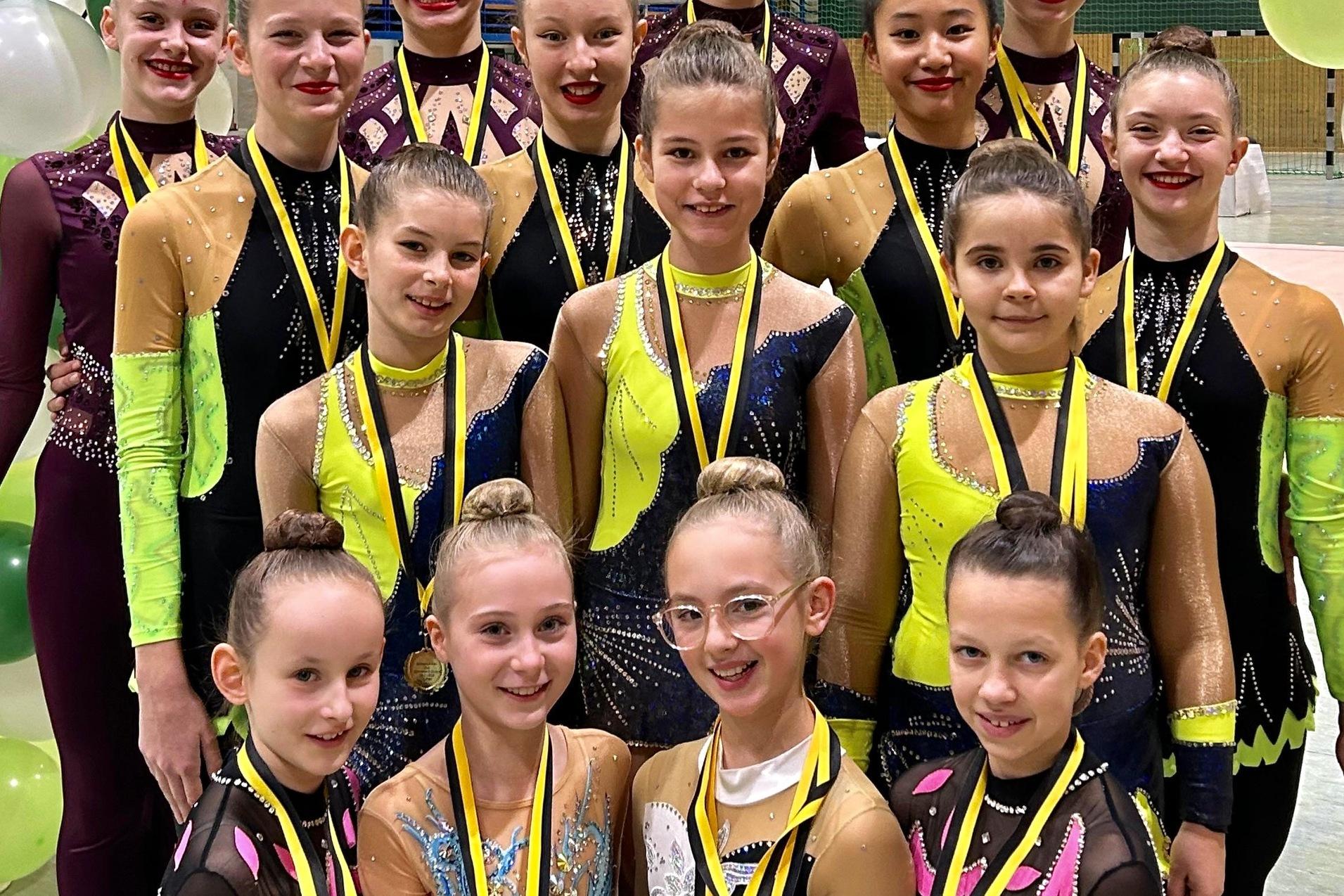 Gruppe von T&auml;nzerinnen in bunten Kost&uuml;men mit Medaillen, stehend vor einem dekorativen Luftballonbogen.