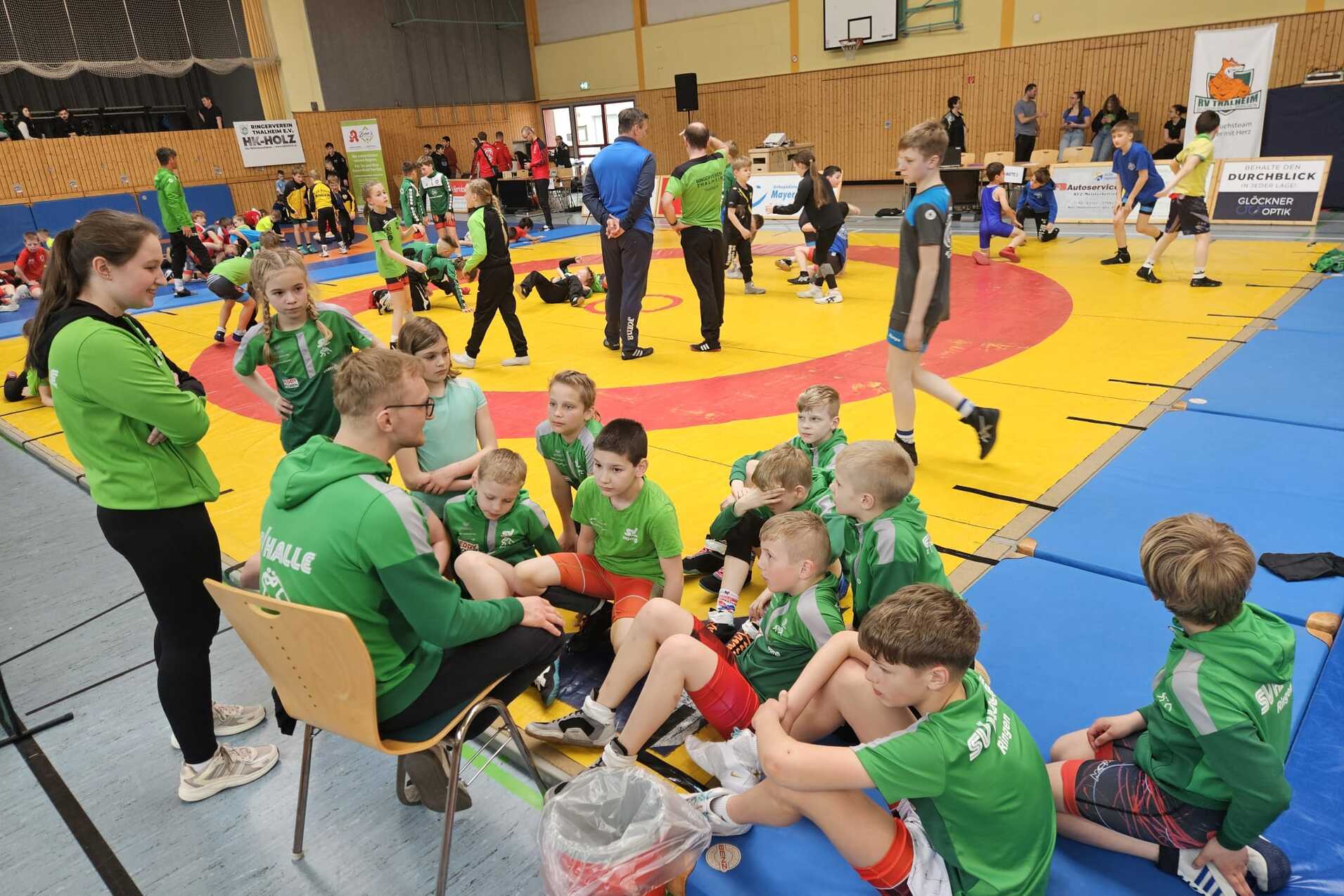 Der Ringernachwuchs sitz auf einer Matte und h&ouml;rt dem Trainer zu.