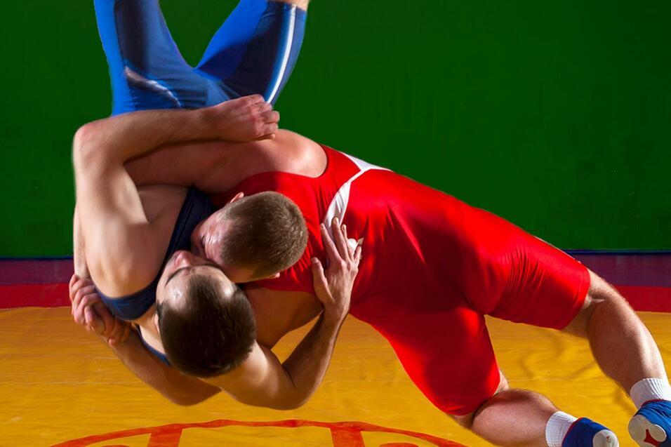 Zwei Ringer kämpfen auf einer gelben Matte, einer im blauen, der andere im roten Anzug, mit grünem Hintergrund.
