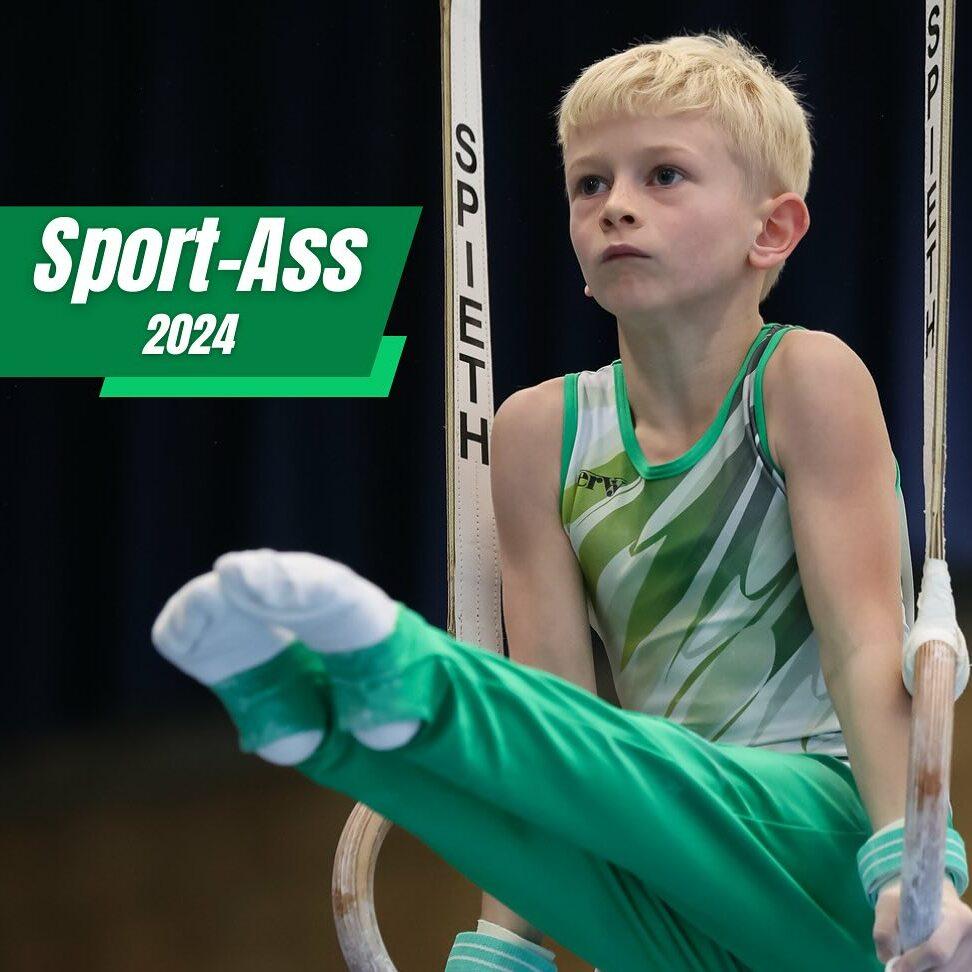 Junge in sportlicher Kleidung übt an Turnringen, sitzt in Gleitposition mit konzentriertem Gesichtsausdruck.