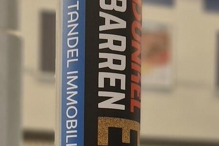 Nahaufnahme eines Aufstellers mit der Aufschrift &bdquo;Goldbarren EM 2025&ldquo; in einer Sporthalle.