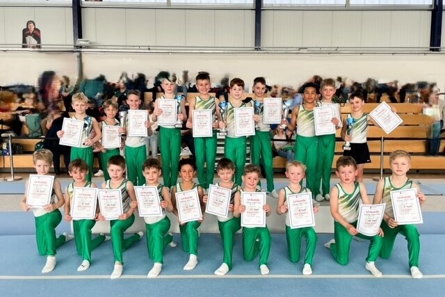 Gruppe von jungen Sportlern in gr&uuml;nen Trikots, die stolz ihre Urkunden in einer Turnhalle pr&auml;sentieren.