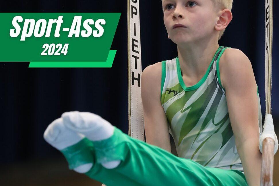 Junge in sportlicher Kleidung &uuml;bt an Turnringen, sitzt in Gleitposition mit konzentriertem Gesichtsausdruck.