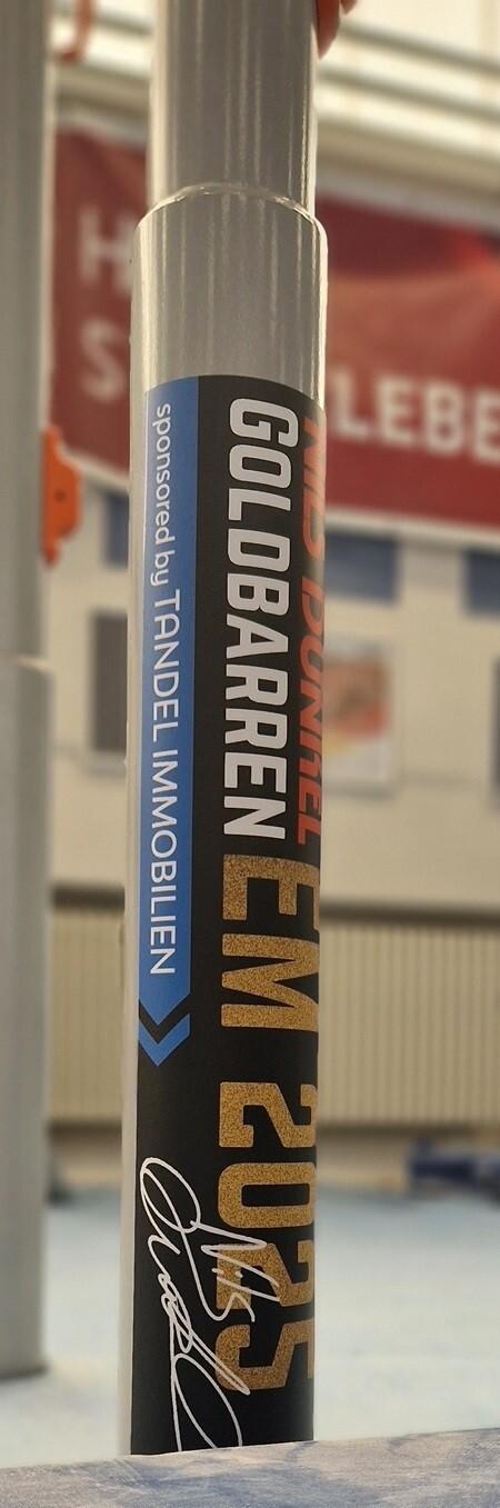 Nahaufnahme eines Aufstellers mit der Aufschrift „Goldbarren EM 2025“ in einer Sporthalle.