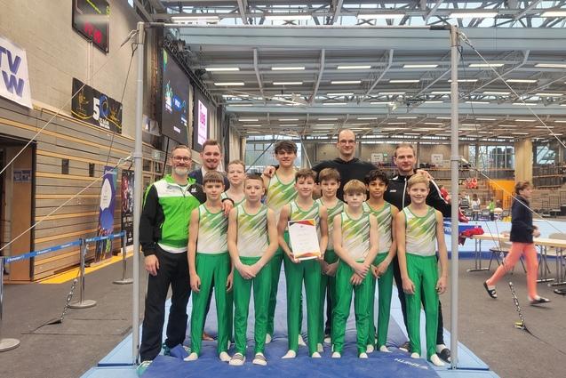 Gruppe von Jungen in Sportkleidung und Trainern, posierend mit einer Urkunde an einem Gymnastikger&uuml;st.