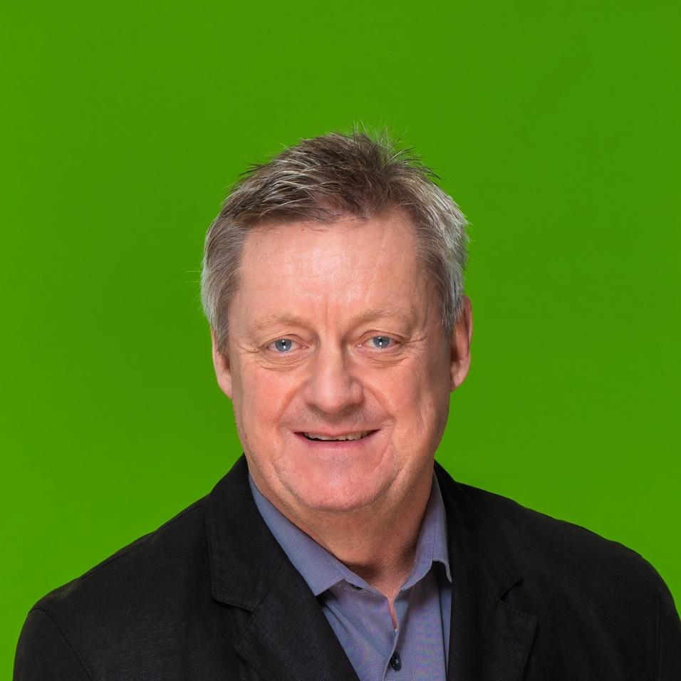 Porträt eines Mannes mit grauen Haaren, in schwarzer Jacke vor grünem Hintergrund, lächelnd und mit neutralem Ausdruck.