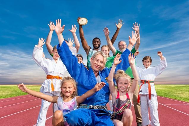 Gruppe von Sportlern in Trainingskleidung, die fröhlich auf einer Laufbahn posieren und die Hände heben.