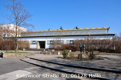 Moderne Geb&auml;ude mit geschwungenem Dach, umgeben von B&auml;umen und einem Platz mit einer Statue in Halle.