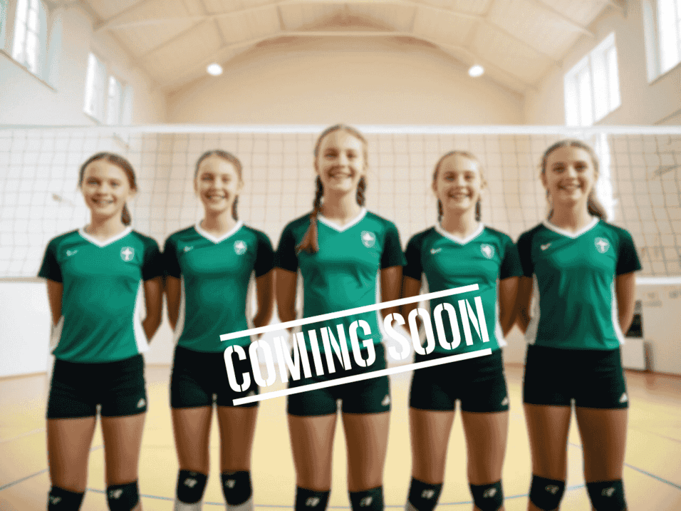 Fünf junge Volleyballspielerinnen in grünen Trikots posieren lächelnd vor einem Volleyballnetz in einer Halle.