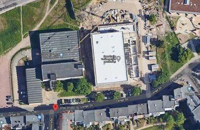 Luftaufnahme eines Baustellenbereichs mit mehreren Geb&auml;uden und Stra&szlig;en in der Umgebung.