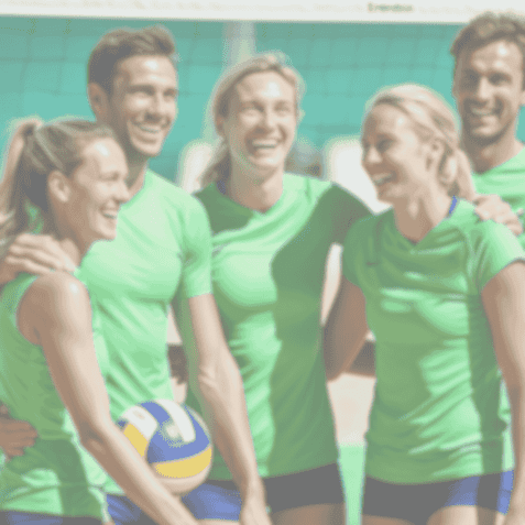 Gruppe von fünf Personen in grünen Trikots, die gemeinsam mit einem Volleyball auf dem Feld lachen und posieren.