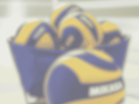 Volleyballs in einer blauen Wanne auf einem Volleyballplatz, mit Netz im Hintergrund.