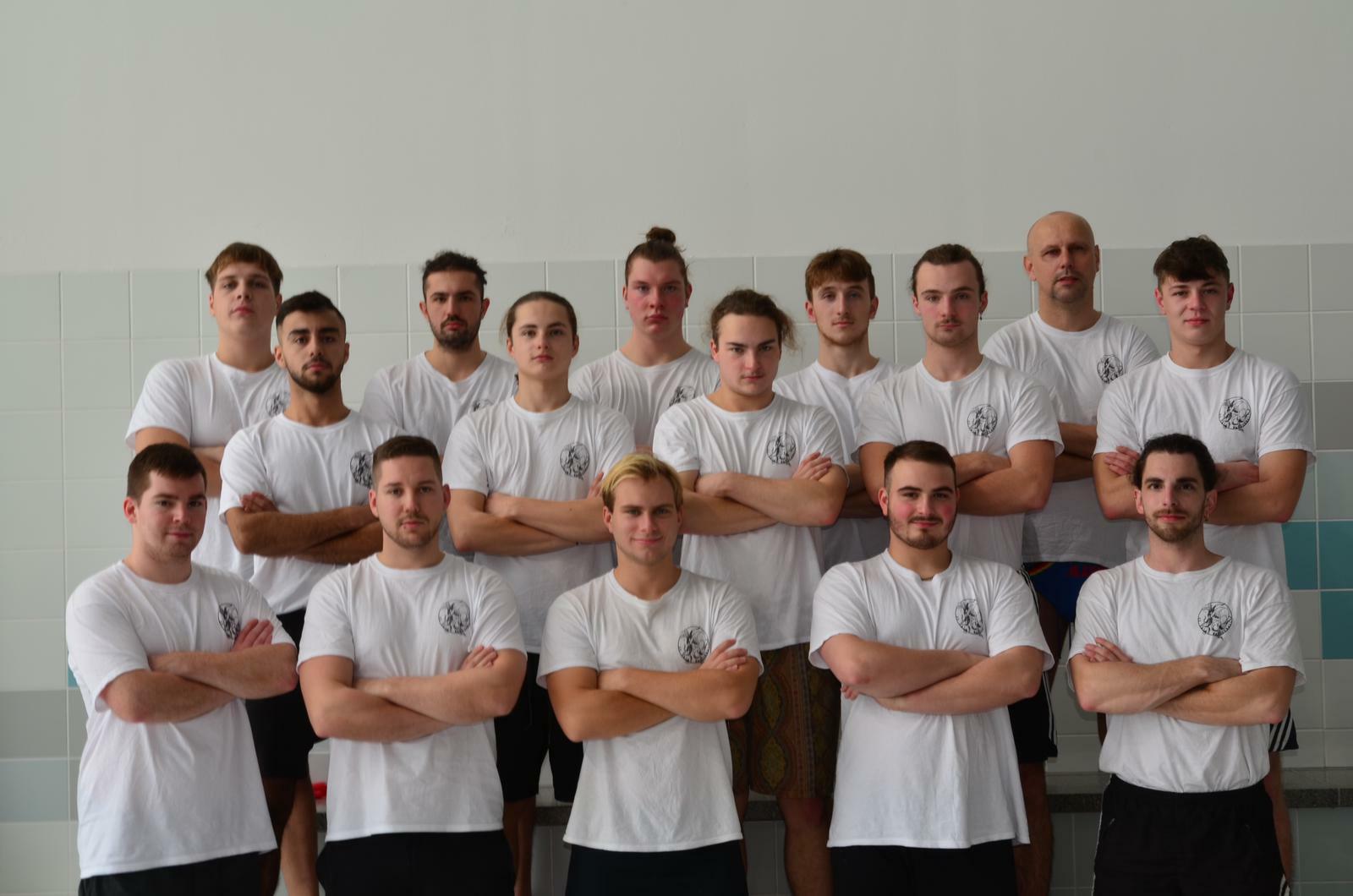 Gruppenfoto von 15 männlichen Sportlern in weißen T-Shirts, stehend und mit verschränkten Armen auf einem Sportgelände.