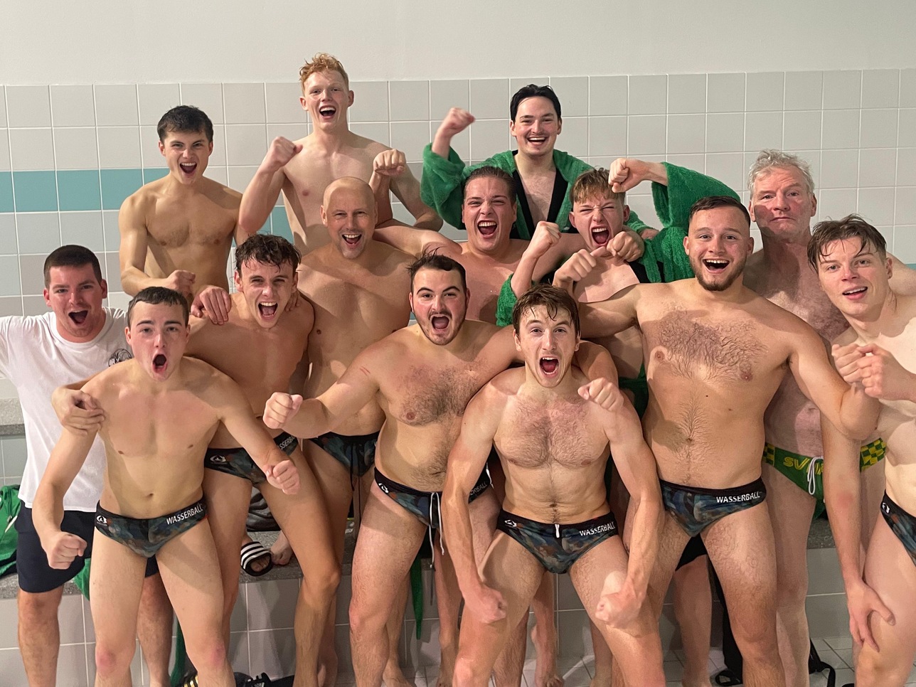 Gruppe von 12 feiernden Wasserballspielern mit fröhlichen Ausdrücken nach dem Wettkampf in einem Schwimmbad.