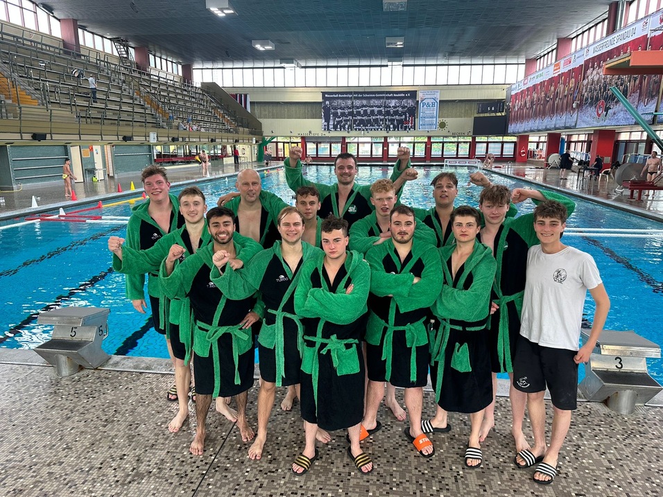 Gruppe von Schwimmern in grünen Badekappen und -mänteln, posierend am Beckenrand eines Schwimmbads.