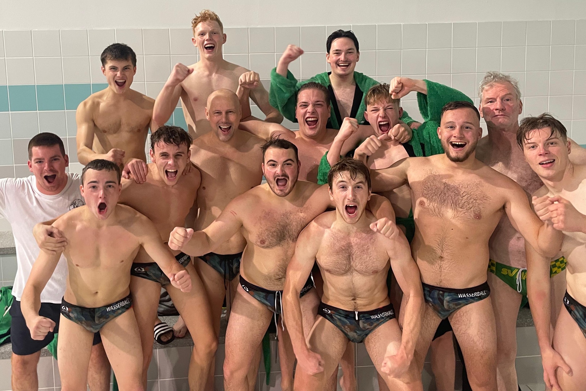 Gruppe von 12 feiernden Wasserballspielern mit fr&ouml;hlichen Ausdr&uuml;cken nach dem Wettkampf in einem Schwimmbad.