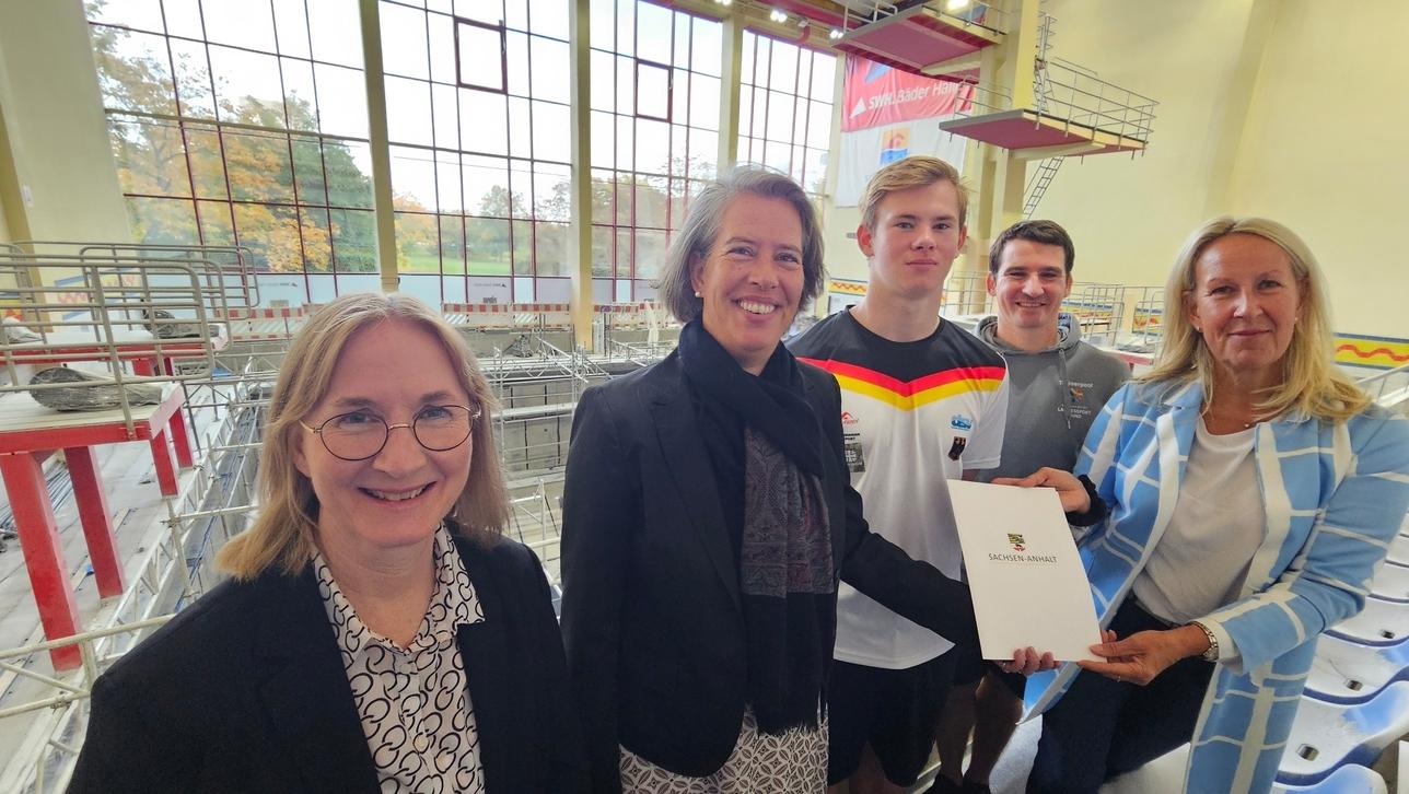 Gruppenfoto mit fünf Personen in einem Schwimmbad, eine Person hält ein Dokument mit dem Logo „Sachsen-Anhalt“.