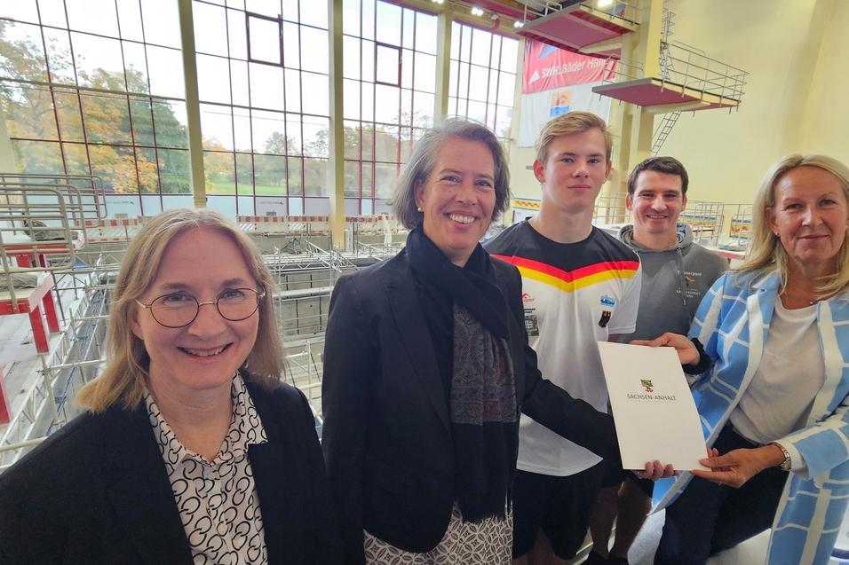 Gruppenfoto mit f&uuml;nf Personen in einem Schwimmbad, eine Person h&auml;lt ein Dokument mit dem Logo &bdquo;Sachsen-Anhalt&ldquo;.