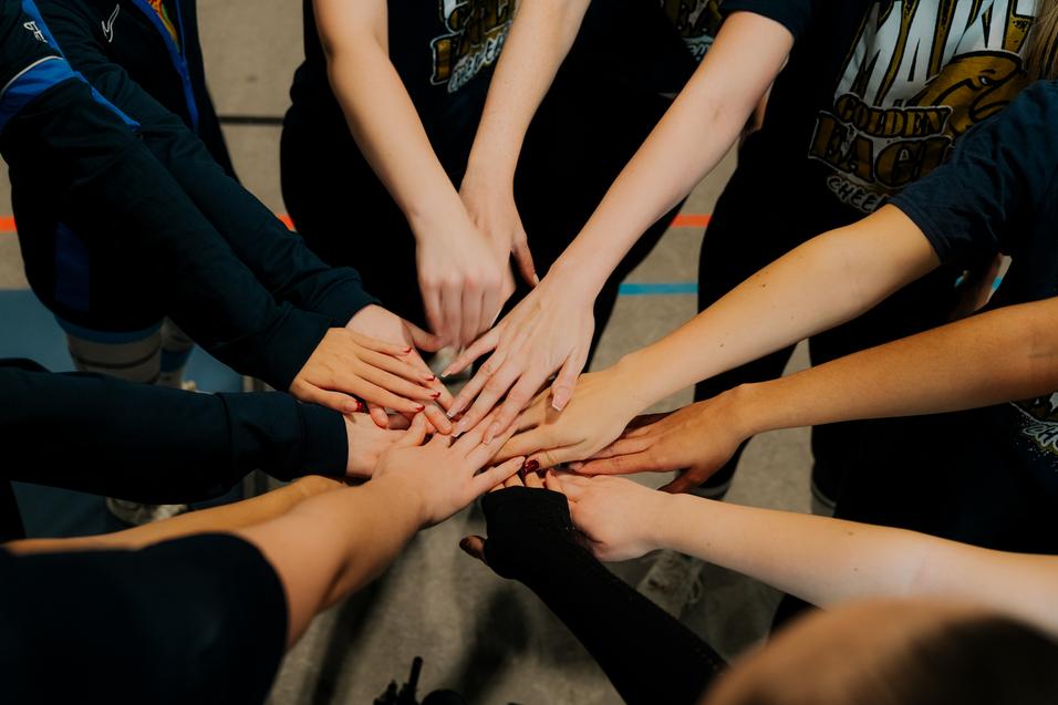 Verschlungene Hände von Cheerleadern bilden einen Kreis auf einem Sportboden, symbolisieren Teamgeist und Zusammenhalt.