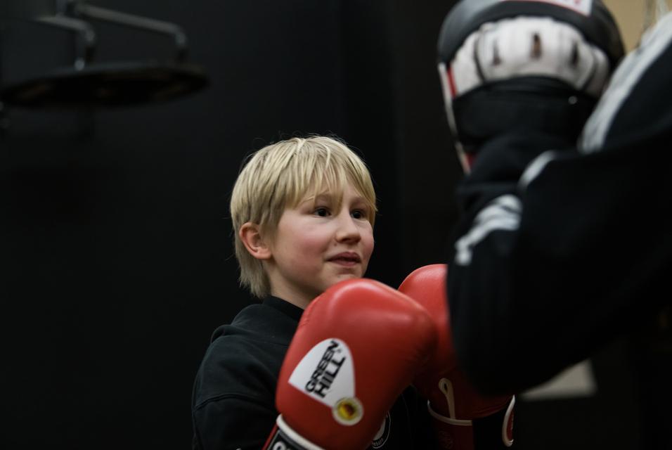 Junger Boxer mit blondem Haar trägt rote Handschuhe und lächelt während des Trainings in einem Sportstudio.