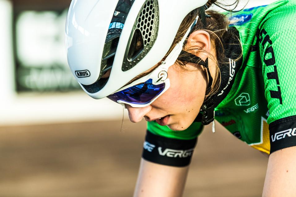 Nahaufnahme einer radfahrenden Sportlerin mit grünem Trikot und weißem Helm, konzentriert auf die Strecke.