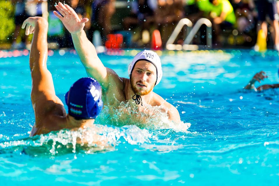 Wasserballspiel mit zwei Spielern im Becken, einer versucht, einen Wurf auszuführen, während der andere verteidigt.